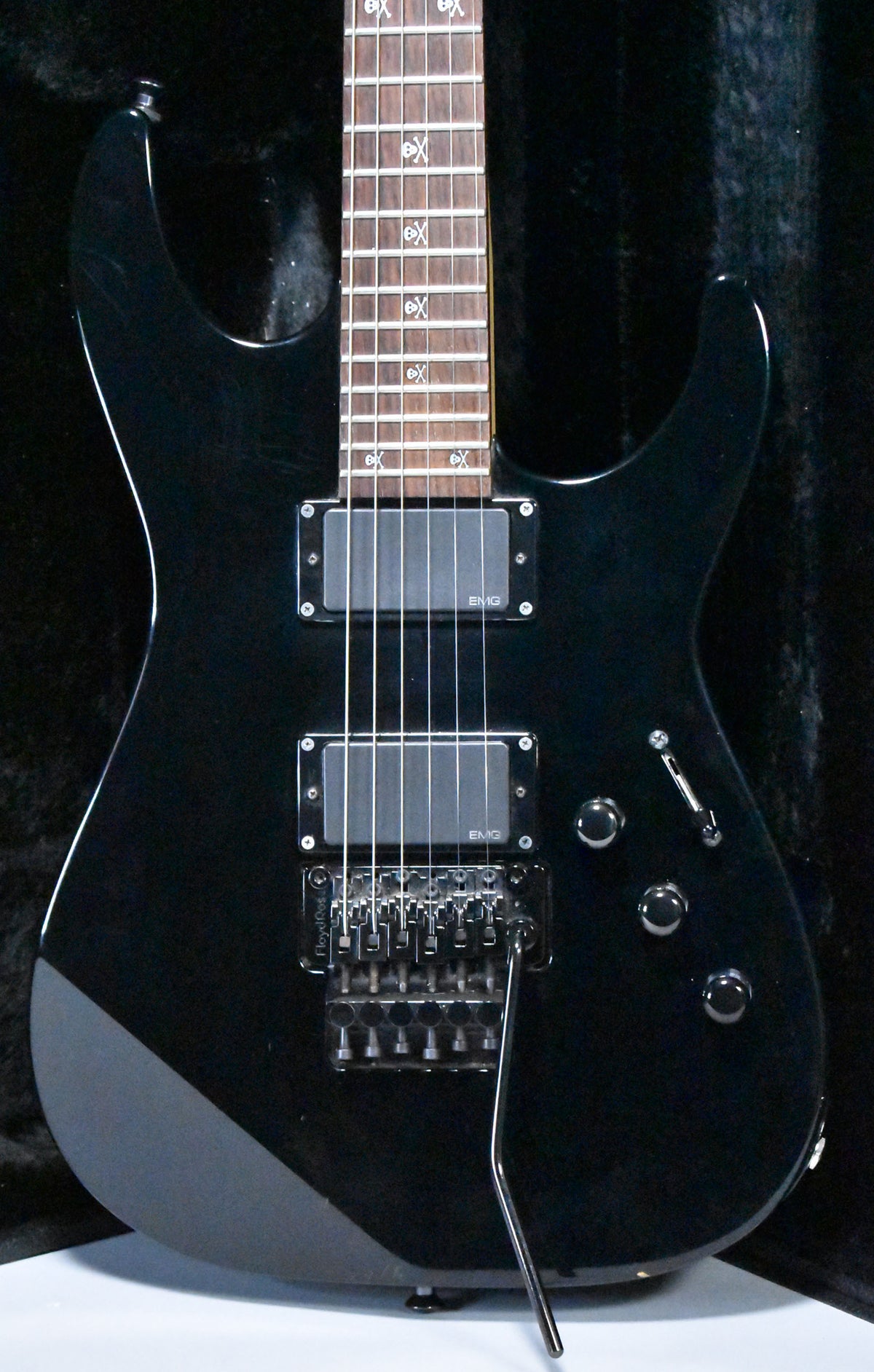 A black electric guitar with a glossy finish, two EMG humbuckers, a Floyd Rose tremolo, and skull-and-crossbones fret inlays.