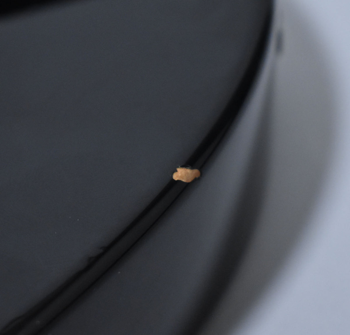 Close-up of a black guitar body's edge, showing a small, irregular chip in the finish revealing the lighter wood underneath.
