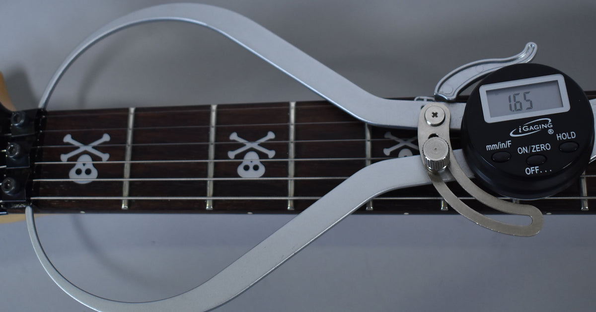 Close-up of the dark fretboard with skull and crossbones inlays, a digital caliper measuring 1.65mm across the frets.