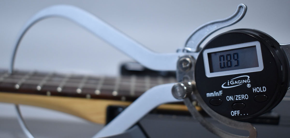 A digital caliper measures the guitar's fret height at 0.89mm, with the dark fretboard and light neck visible in the background.