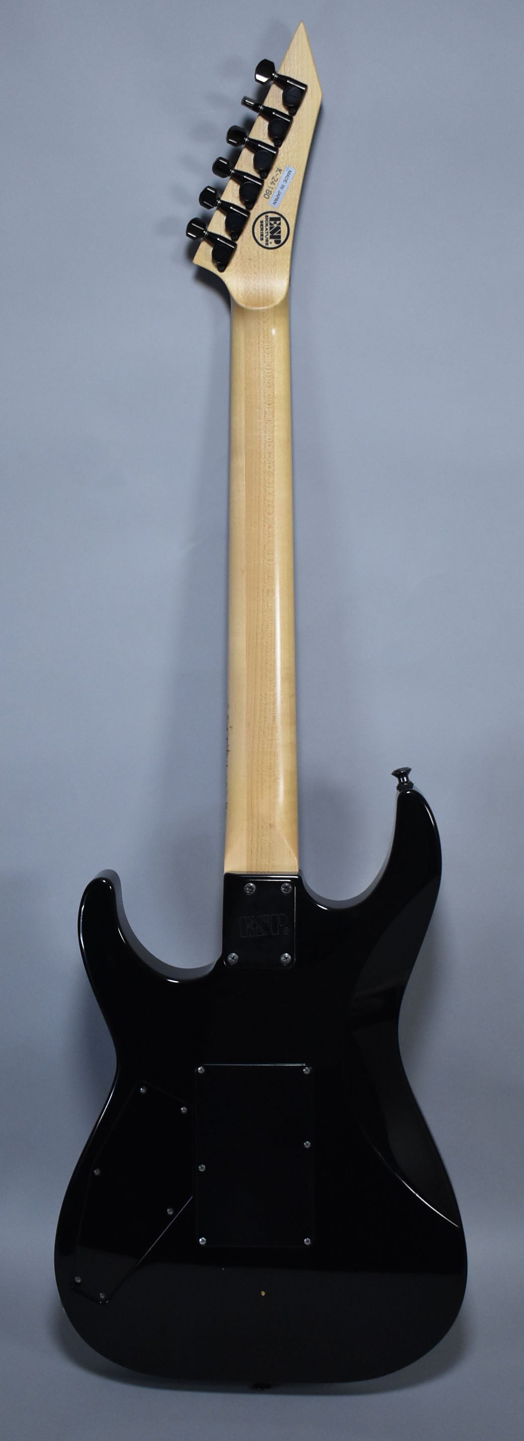 The back of a glossy black electric guitar with a light wood neck and black tuners, showing a small ding on the lower body.