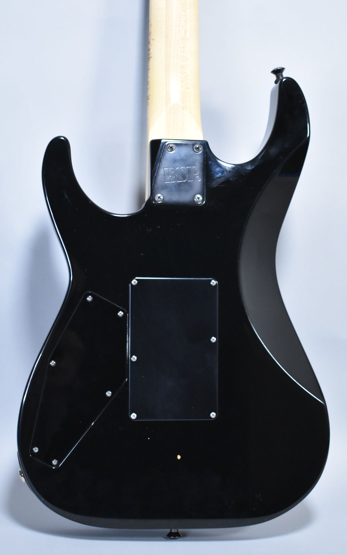 The guitar's glossy black back shows a light-colored maple neck, two black control cavity covers, and a small ding near the bottom.