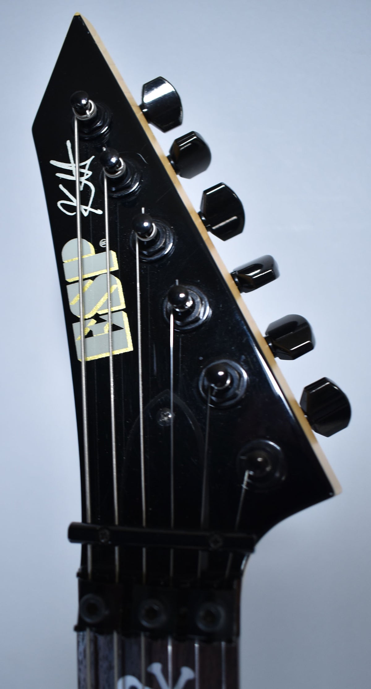 Close-up of the black headstock, angled right, showing six black tuners, a locking nut, and a white signature.