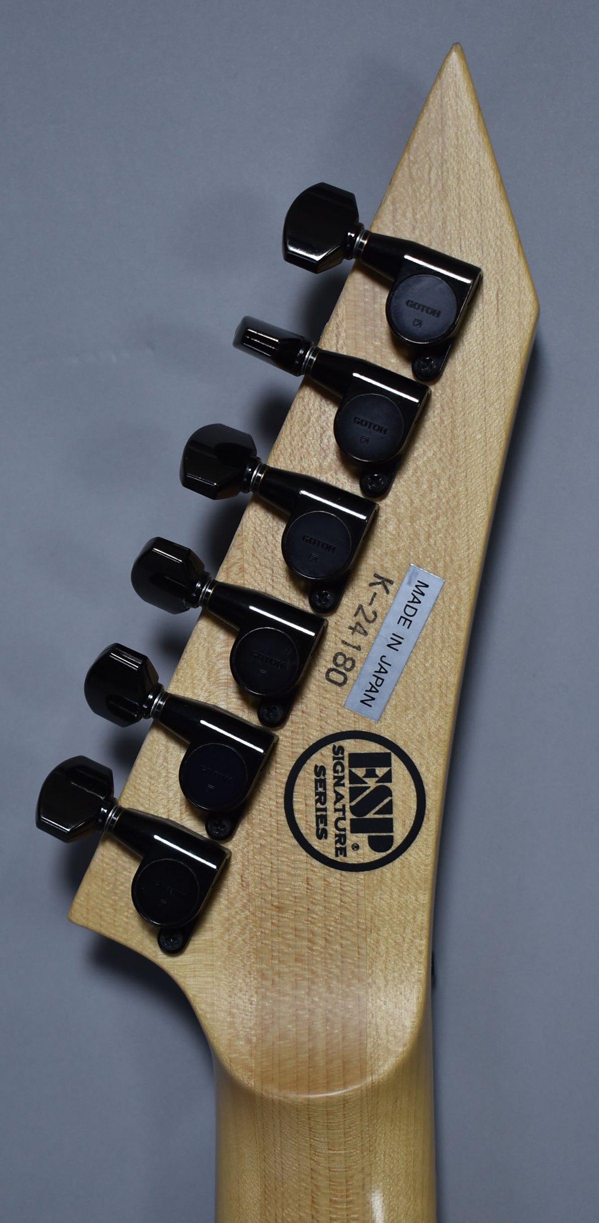 The back of the guitar's natural wood headstock and neck joint, showing six black tuning pegs and a "Made in Japan" sticker.