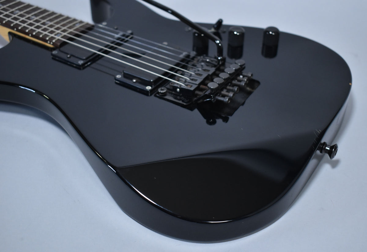 Upper body of a glossy black electric guitar, showing two humbuckers, a Floyd Rose tremolo, and three black control knobs.