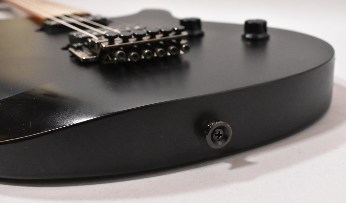 Close-up of the satin black guitar body, showing the output jack, a control knob, and the bridge with fine tuners.
