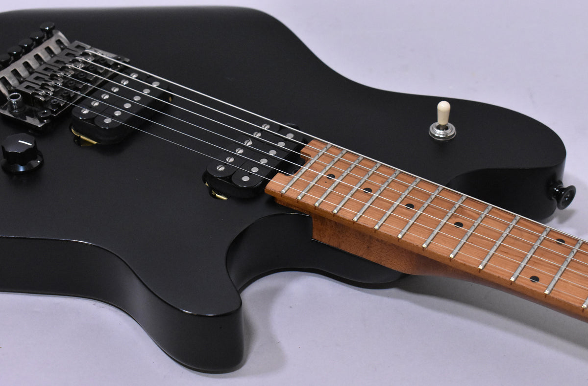 The satin black guitar body, with a natural wood neck and fretboard, features two humbucker pickups and a Floyd Rose tremolo system.