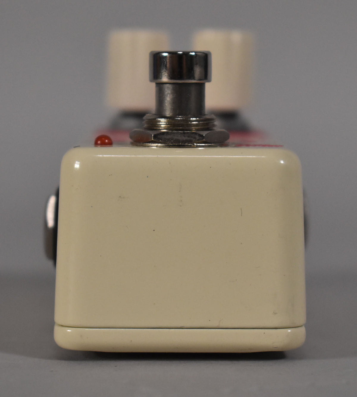 The cream-colored pedal is viewed from the front, showing a chrome footswitch and a small red indicator light.