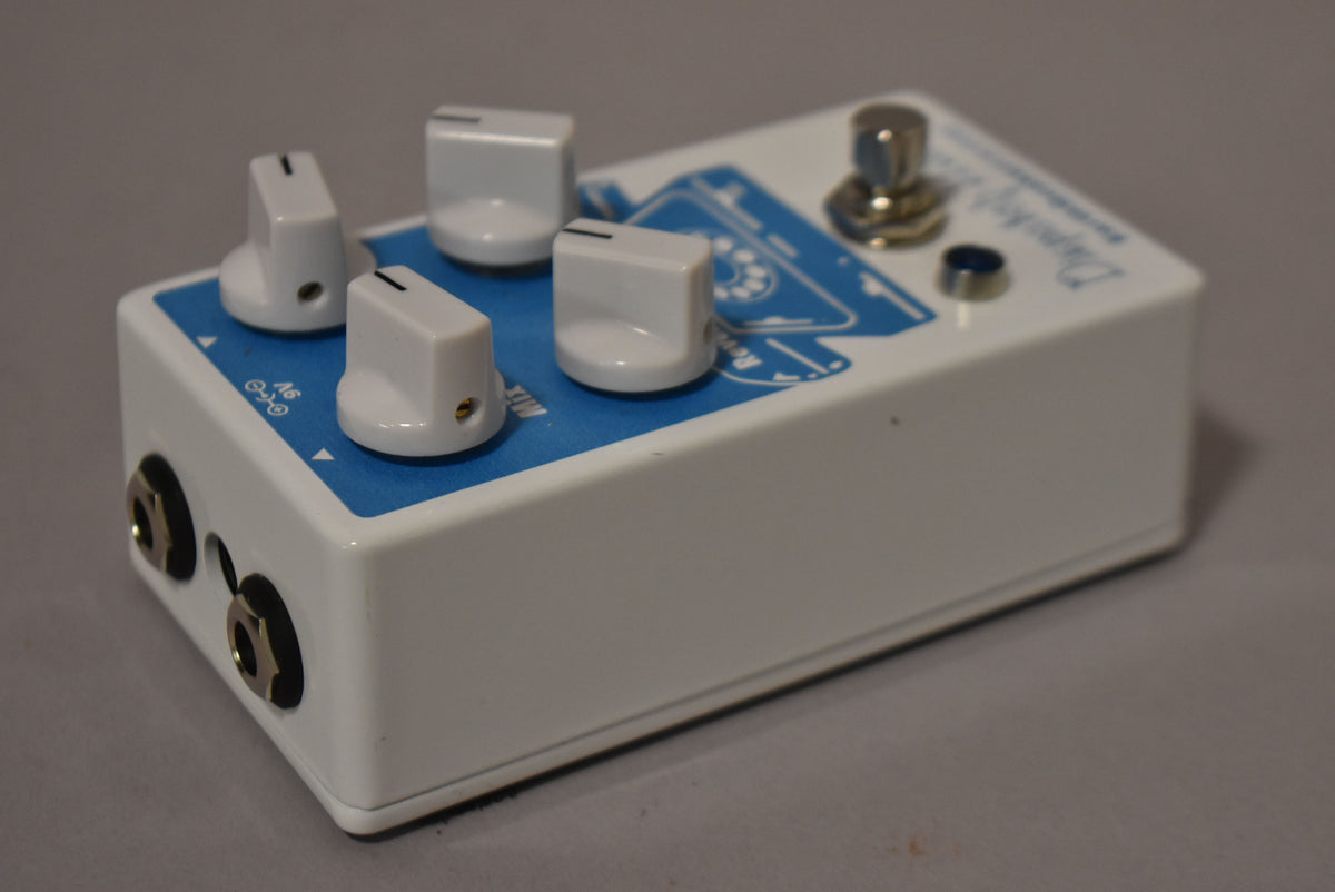 A white effect pedal with a blue top panel, four white knobs, a chrome footswitch, and two input jacks on the left side.
