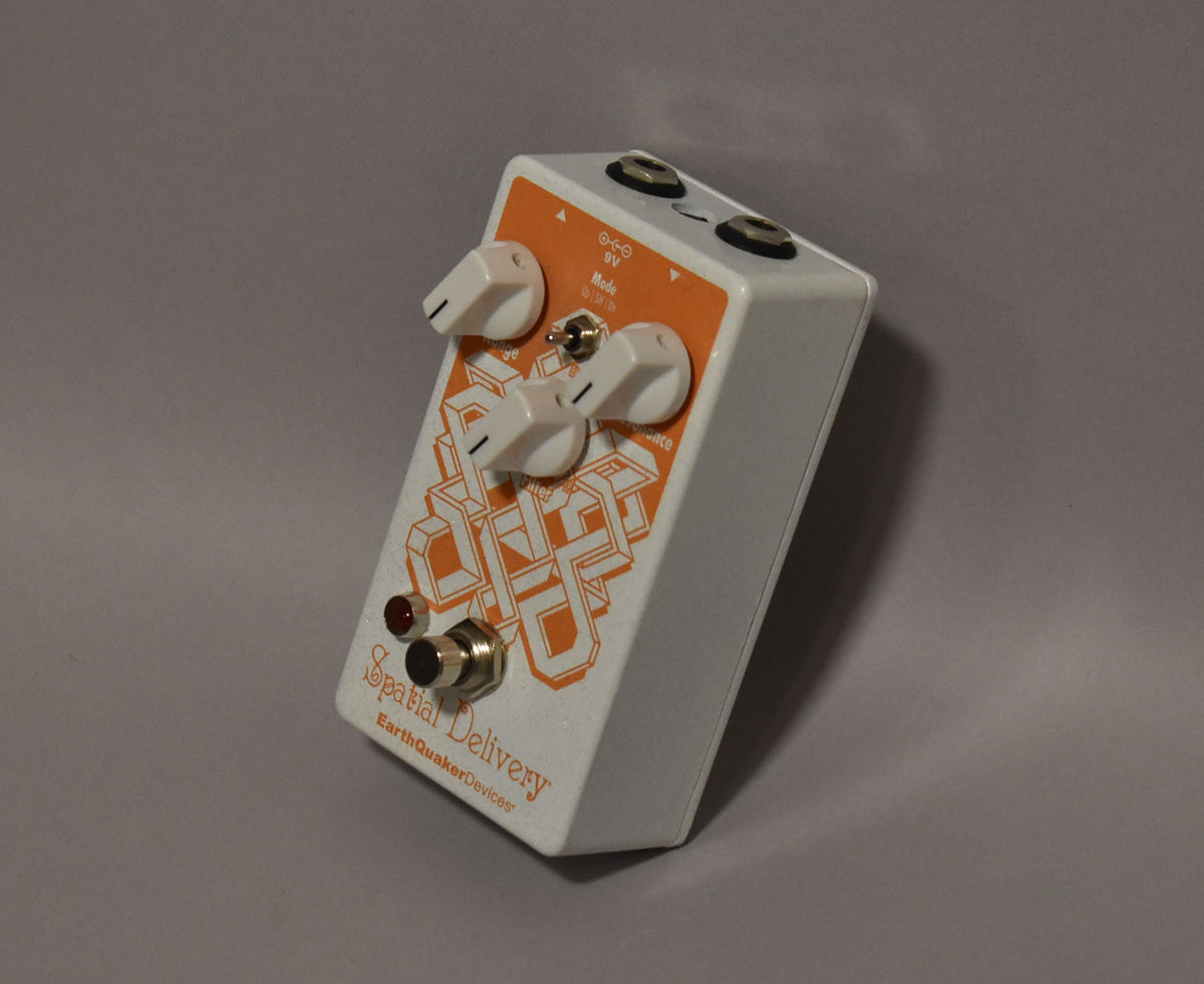 White effects pedal, angled top-down view, with an orange geometric pattern, four white knobs, a toggle switch, and a red LED.