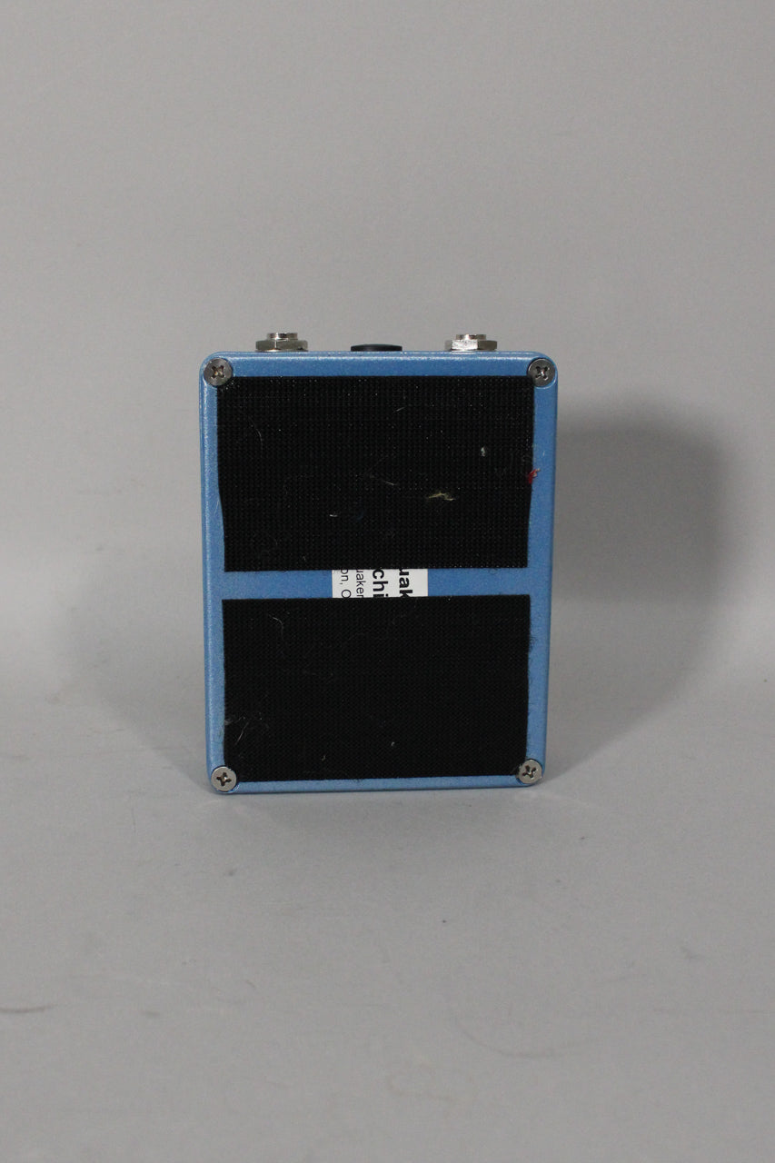 The light blue pedal is seen from the back, with two black velcro strips and a partial white label on the base.