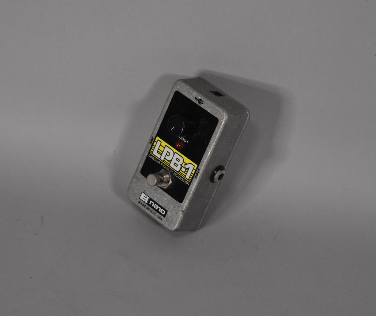 A small, silver-gray metal pedal with a black control panel, one black knob, and a silver footswitch, viewed from above at an angle.