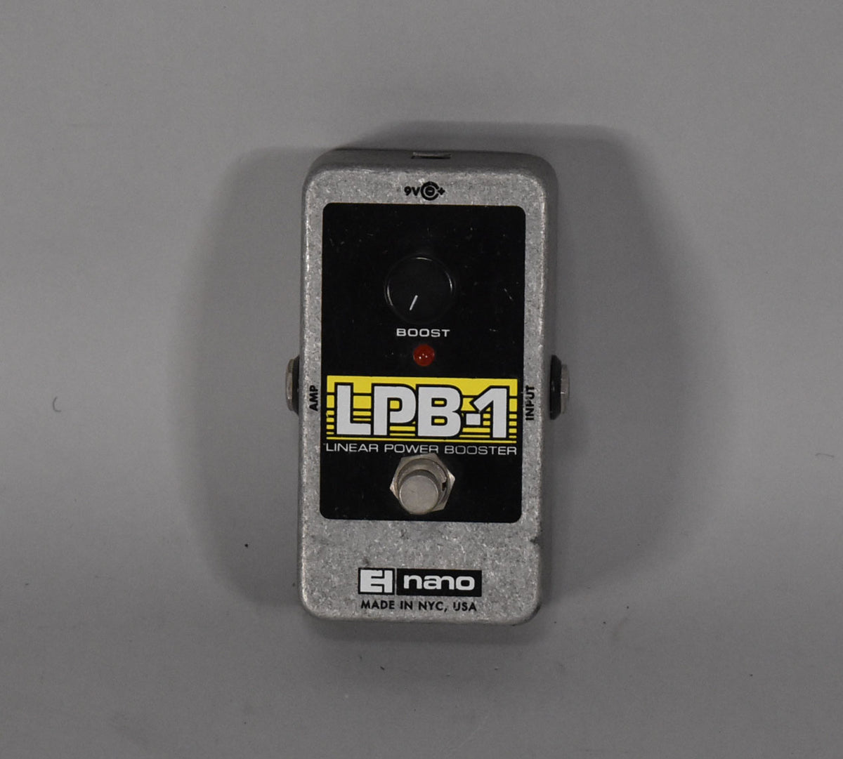 Top-down view of a rectangular silver pedal with a black face, a single black knob, a red LED, and a silver footswitch.