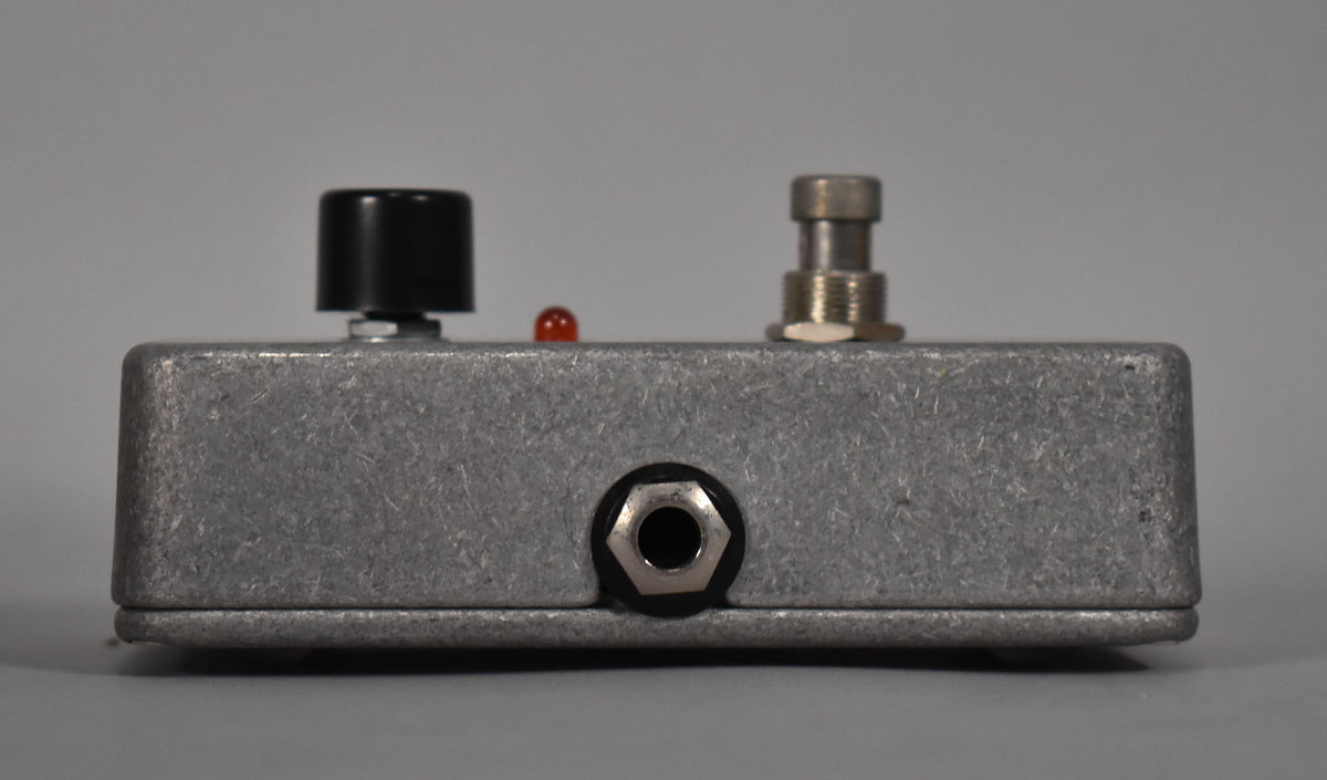 Side view of a textured silver-grey pedal with a black knob, a red LED, a silver footswitch, and a silver input jack.