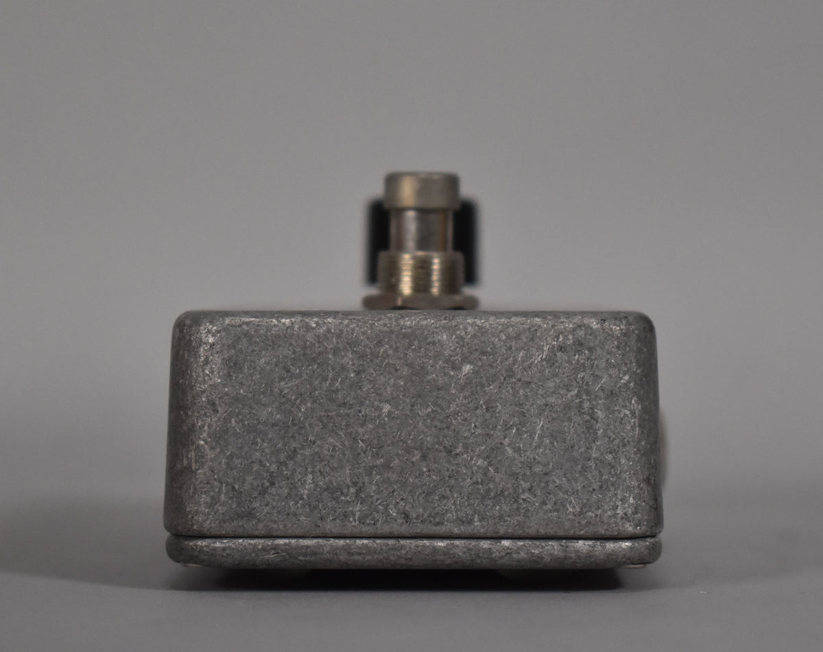 The pedal is viewed from the side, showing its textured, dark gray metal casing and a single silver footswitch.