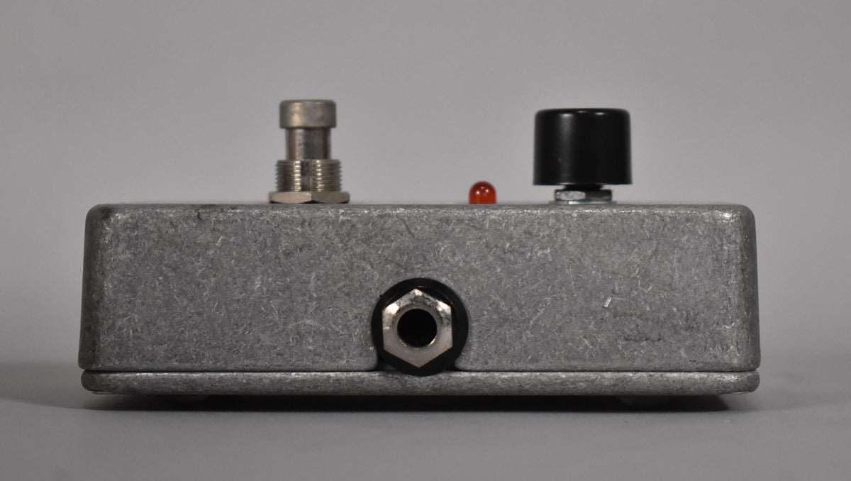 A gray guitar pedal with a silver footswitch, a red indicator light, a black knob, and a 1/4-inch input jack.