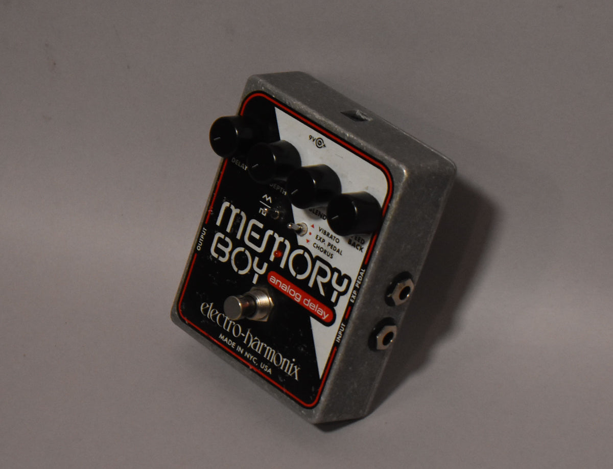 Angled view of a gray, textured pedal with a black and white faceplate, four black knobs, a chrome footswitch, and two input jacks.