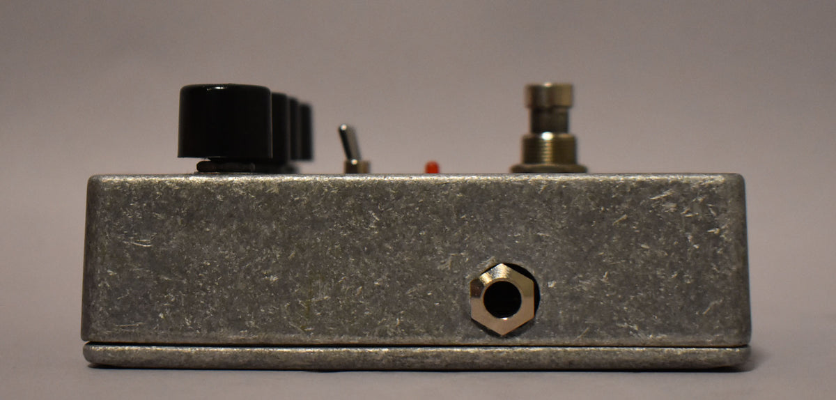 The pedal's right side, with a textured gray finish, shows a 1/4-inch input jack and the edge of three black knobs.