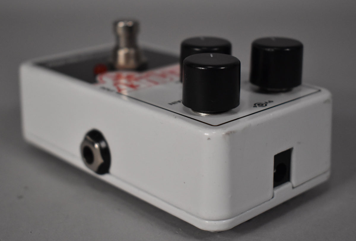 A white pedal, viewed from the right side, showing three black control knobs, a footswitch, an input jack, and a power input.