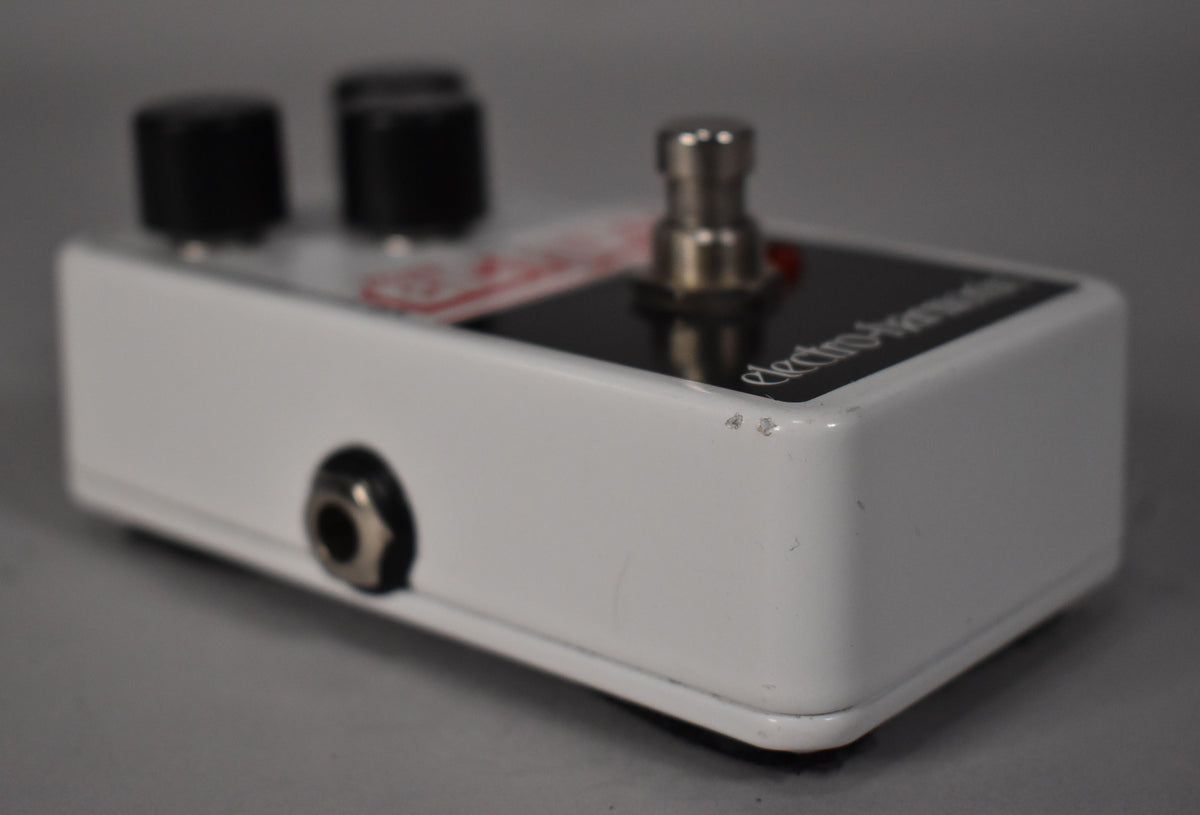 The white pedal is angled right, showing the input jack, two black knobs, a silver footswitch, and minor scuffs on the top right edge.