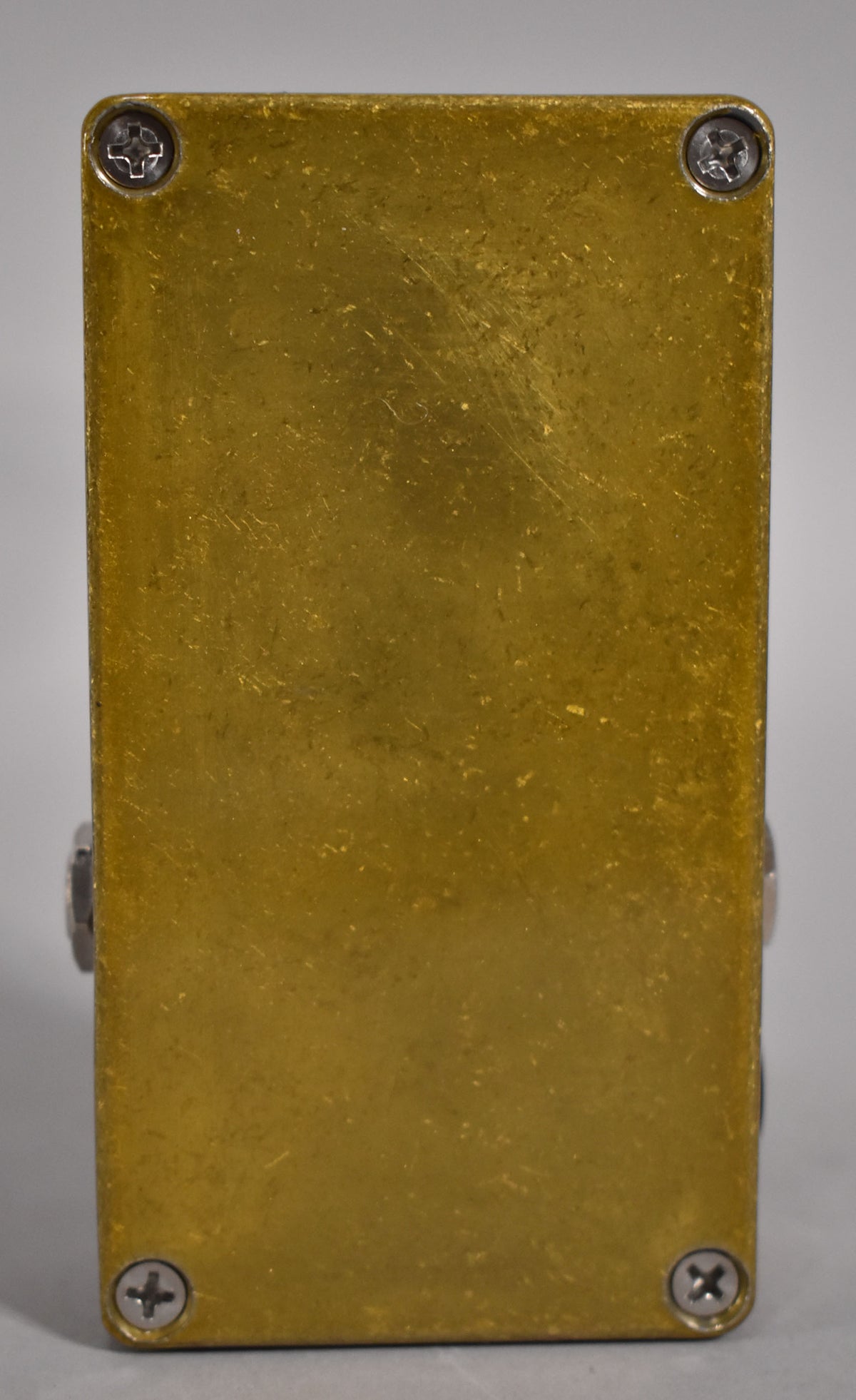 The gold effects pedal is viewed from the bottom, showing a brushed finish with light scratches and four silver Phillips head screws.