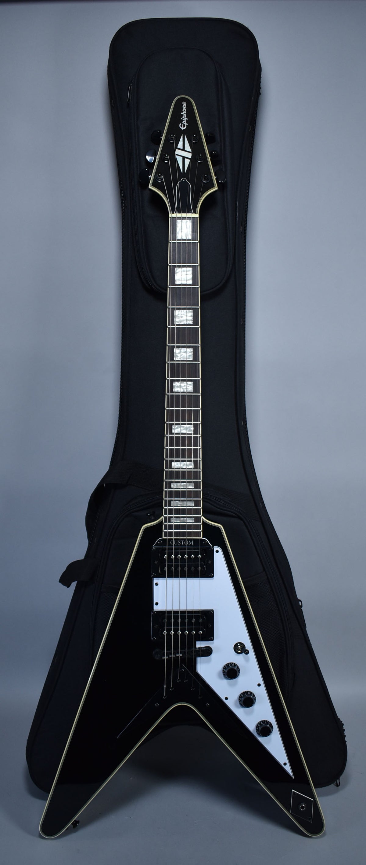 Full-length view of a glossy black Flying V electric guitar with white binding, a white pickguard, and black hardware, resting in a soft case.