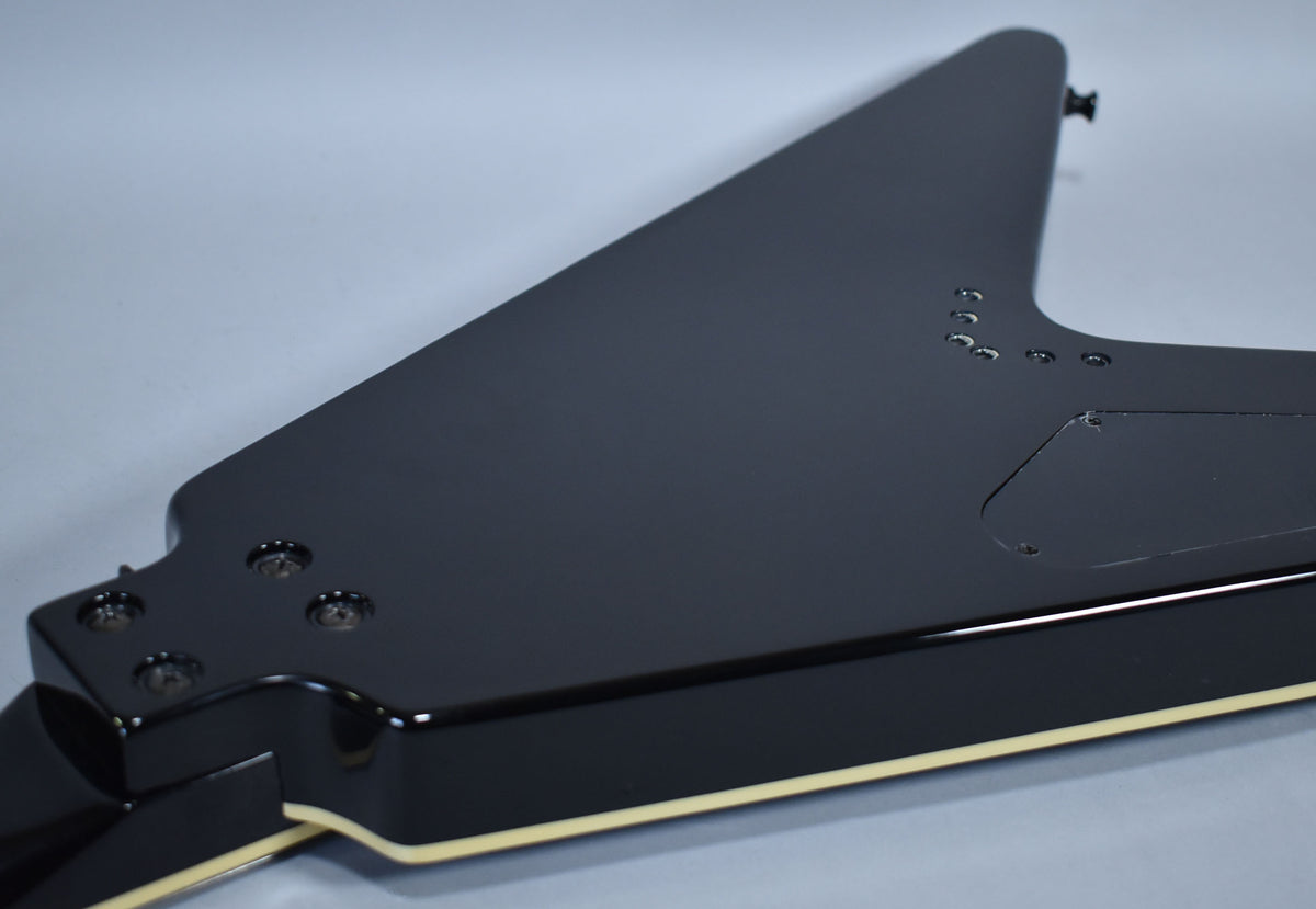 The back of a glossy black Flying V guitar, showing the neck joint, control cavity cover, and string ferrules.