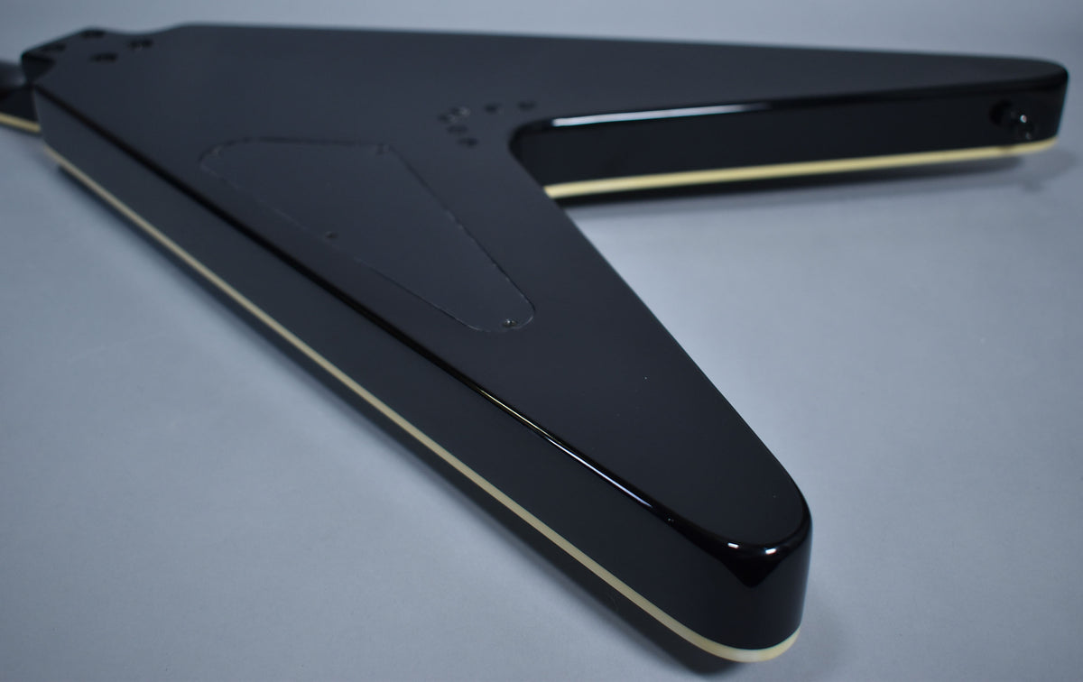 The glossy black Flying V body is angled, showing the cream binding along the edges and the control cavity cover on the back.