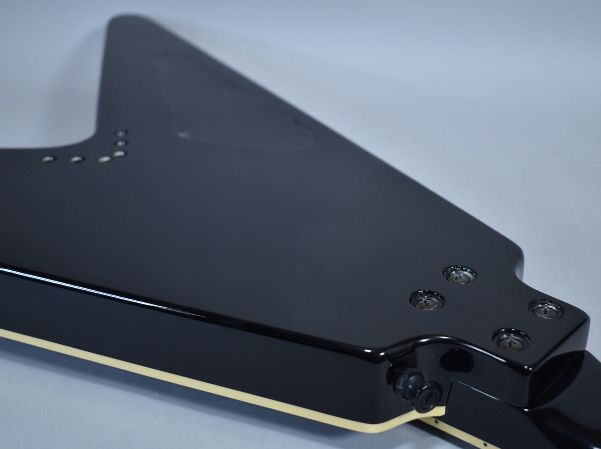 The glossy black Flying V body, with cream binding, is angled from the headstock, showing the back of the tuners.