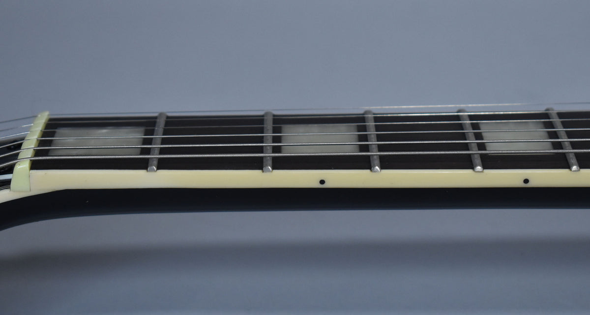 Close-up of the ebony fretboard with rectangular pearloid inlays, cream binding, and a white nut.