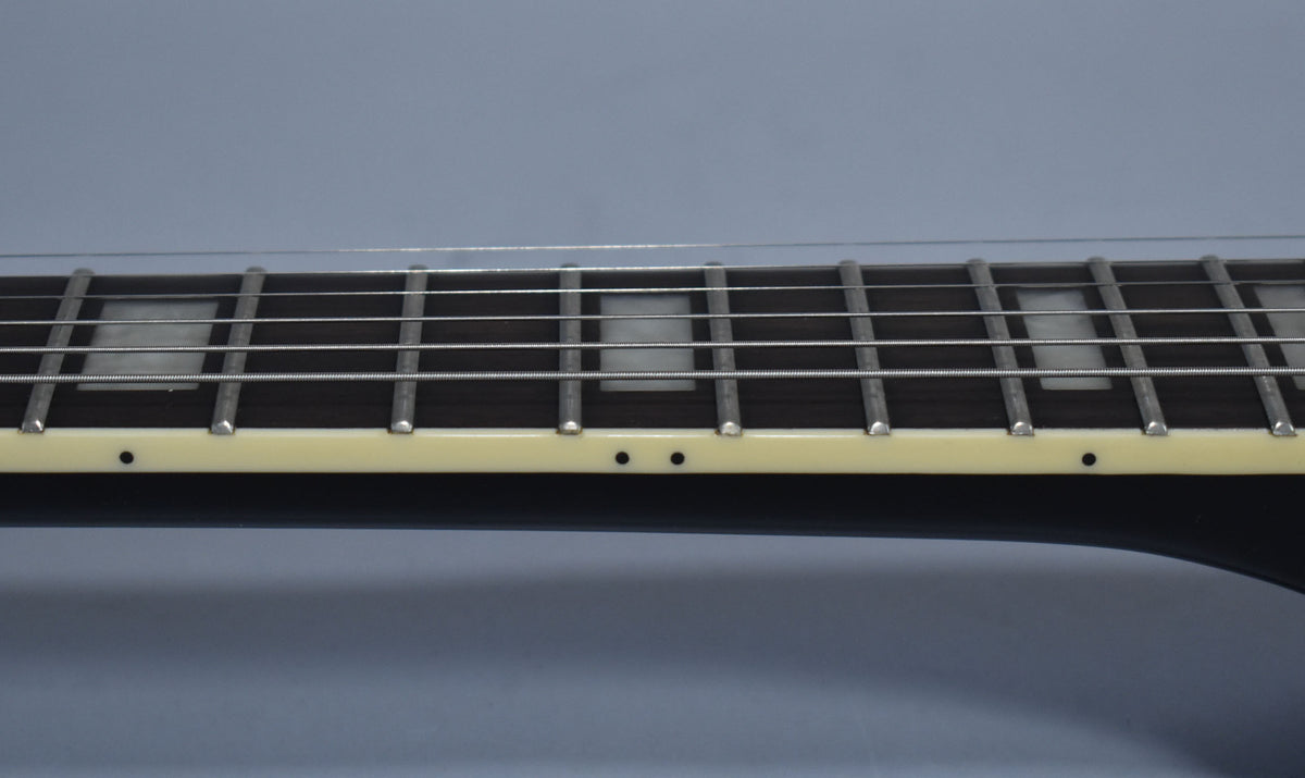 Close-up of the ebony fretboard with rectangular pearloid inlays and cream binding, showing light fret wear.
