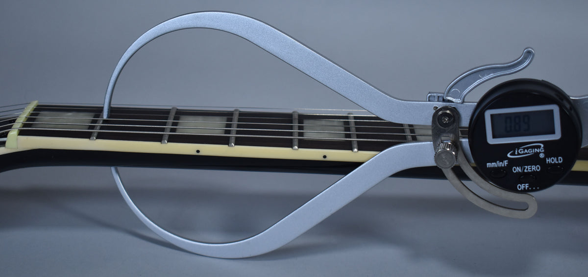 A digital caliper measures the string height above the frets on the ebony fretboard with block inlays.