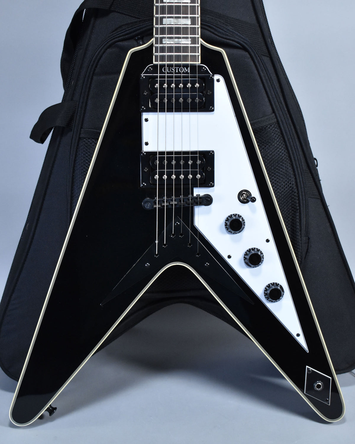 Full front view of a glossy black Flying V electric guitar with a white pickguard, two humbuckers, and three black control knobs.