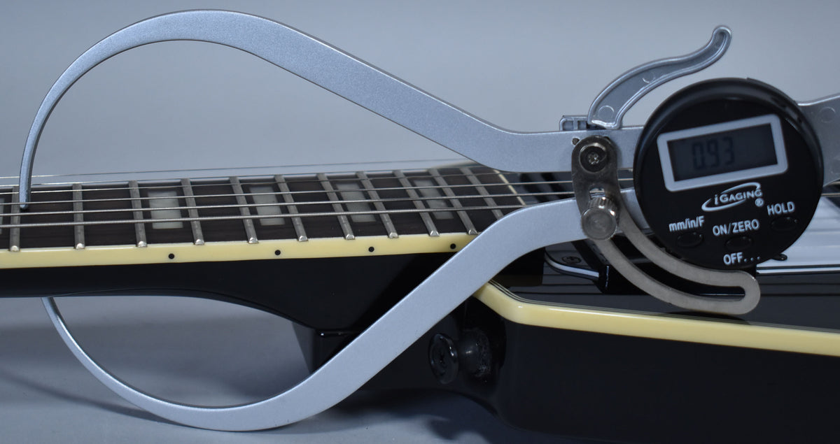 A digital caliper measures the string height above the frets on the ebony guitar's bound fretboard, showing 0.93mm.