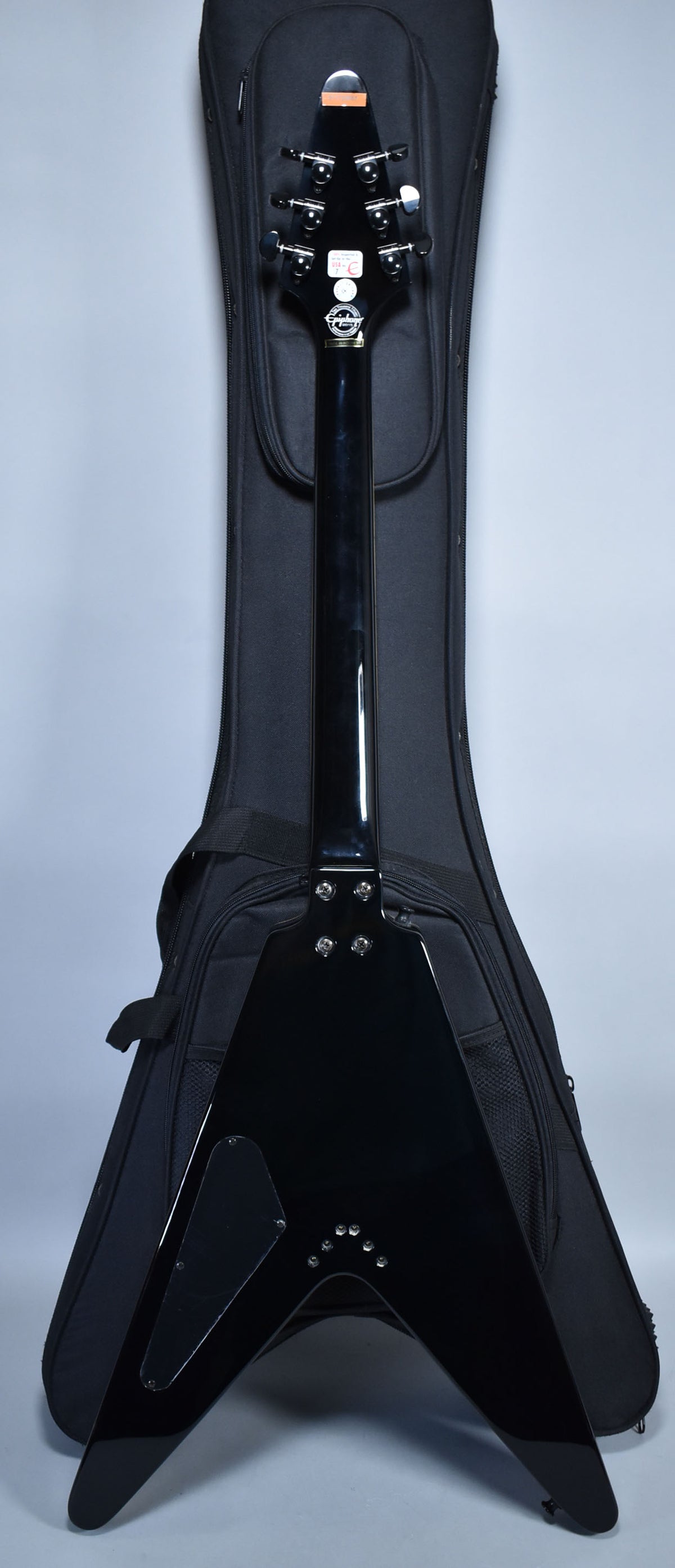 The back of a glossy black Flying V guitar, showing the headstock, neck, and body, with a black soft case behind it.