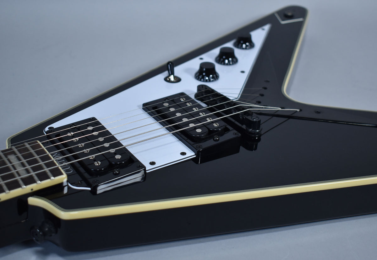 Close-up of the glossy black Flying V body, showing the white pickguard, black humbuckers, and four black control knobs.