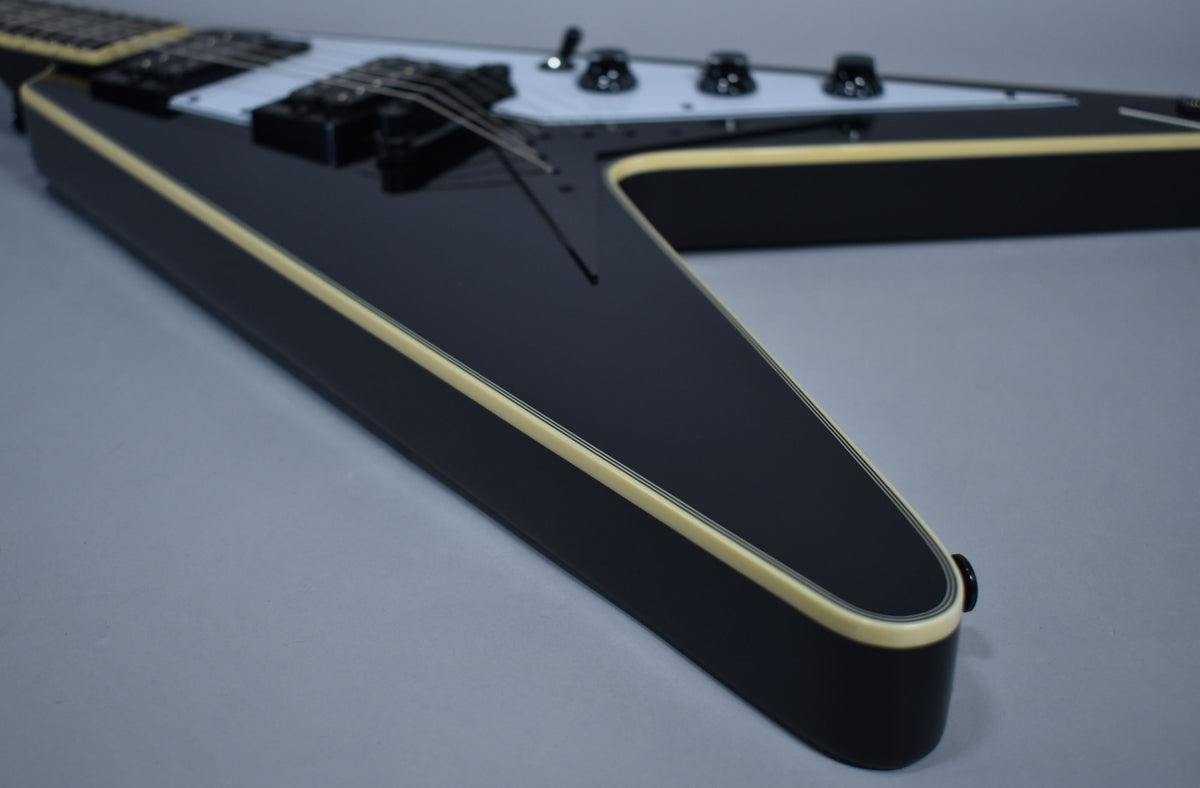 The lower wing of a glossy black Flying V, showing cream binding and a white pickguard with black controls.