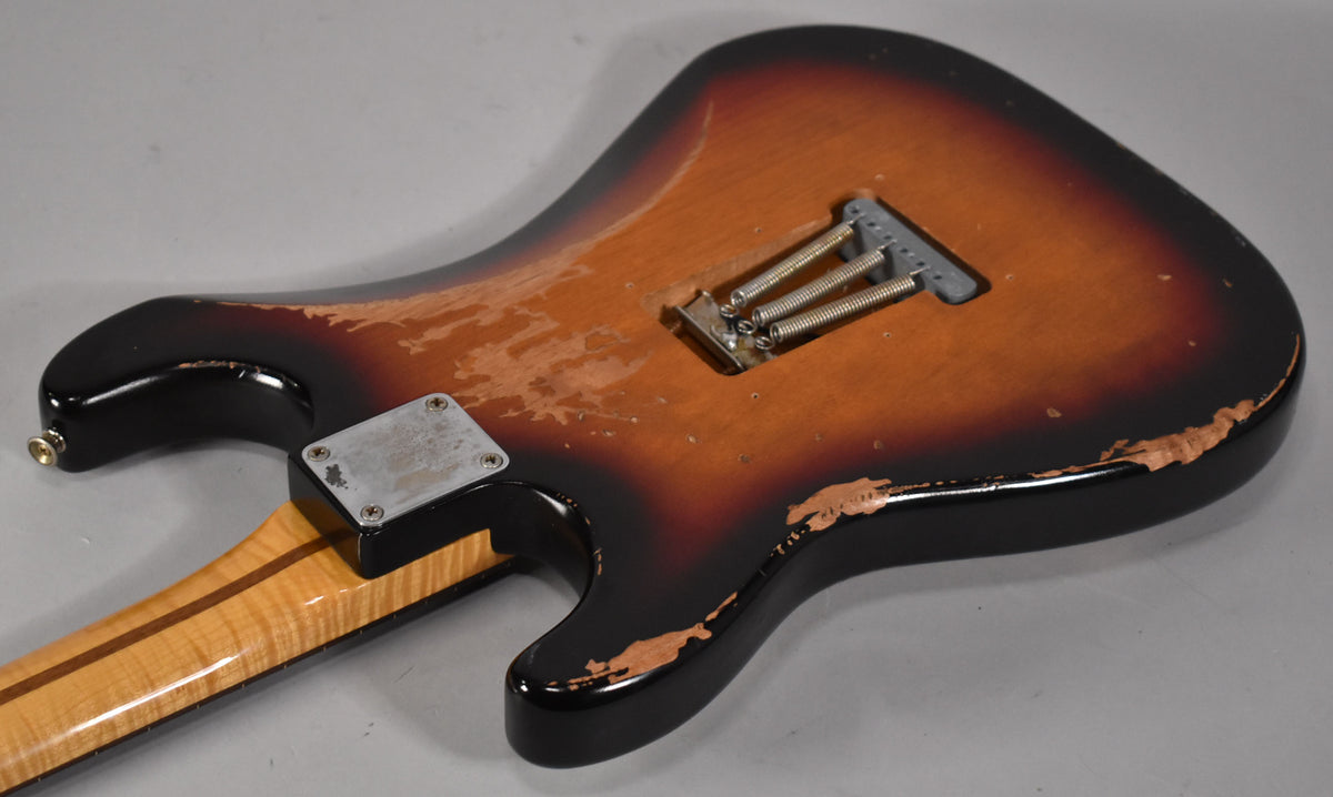 The guitar's sunburst back shows heavy wear, exposing wood, with a tremolo spring cavity and a worn neck plate.