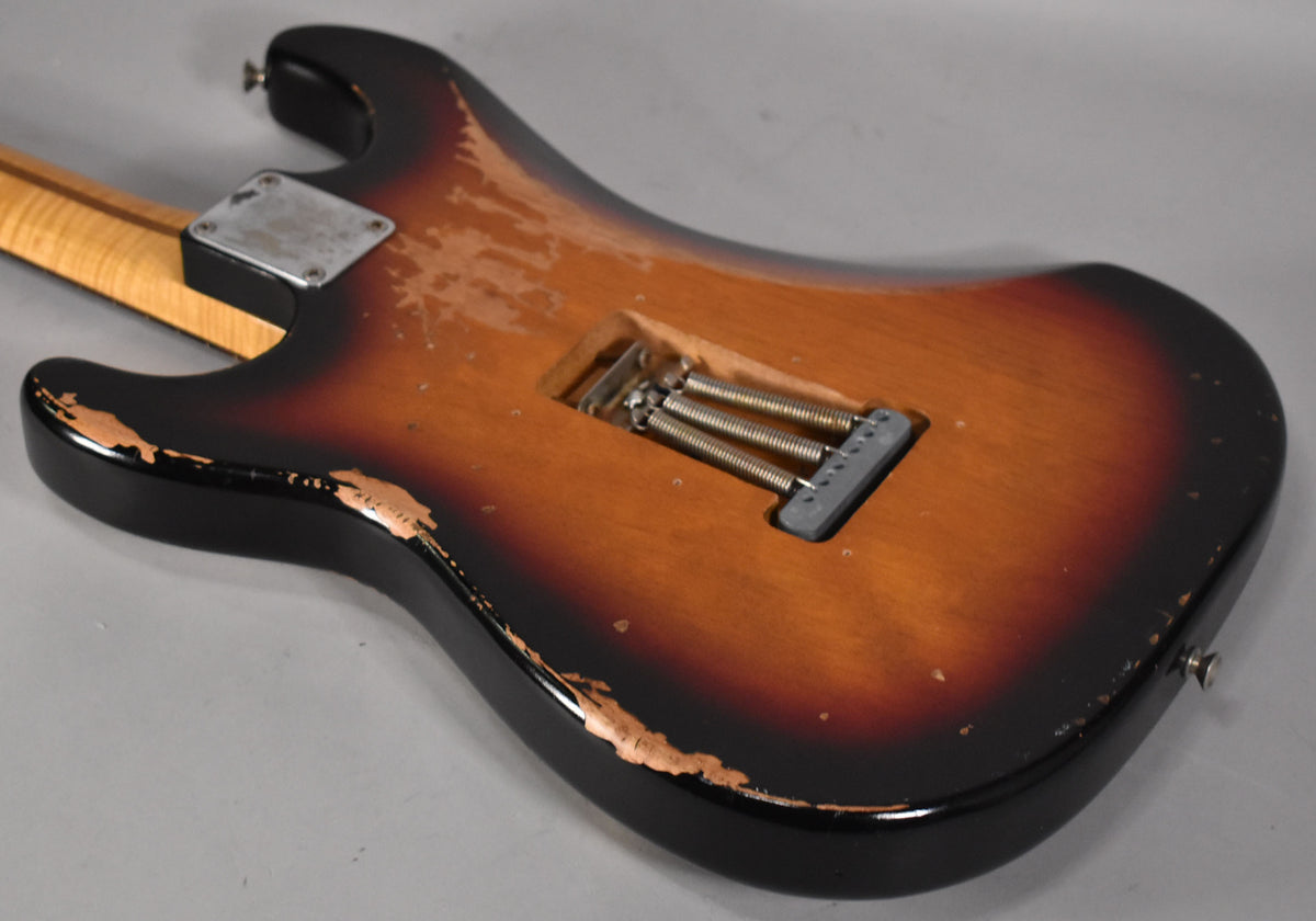 The sunburst S-style guitar's back, showing heavy relic wear, a neck plate, and the tremolo spring cavity with three springs.