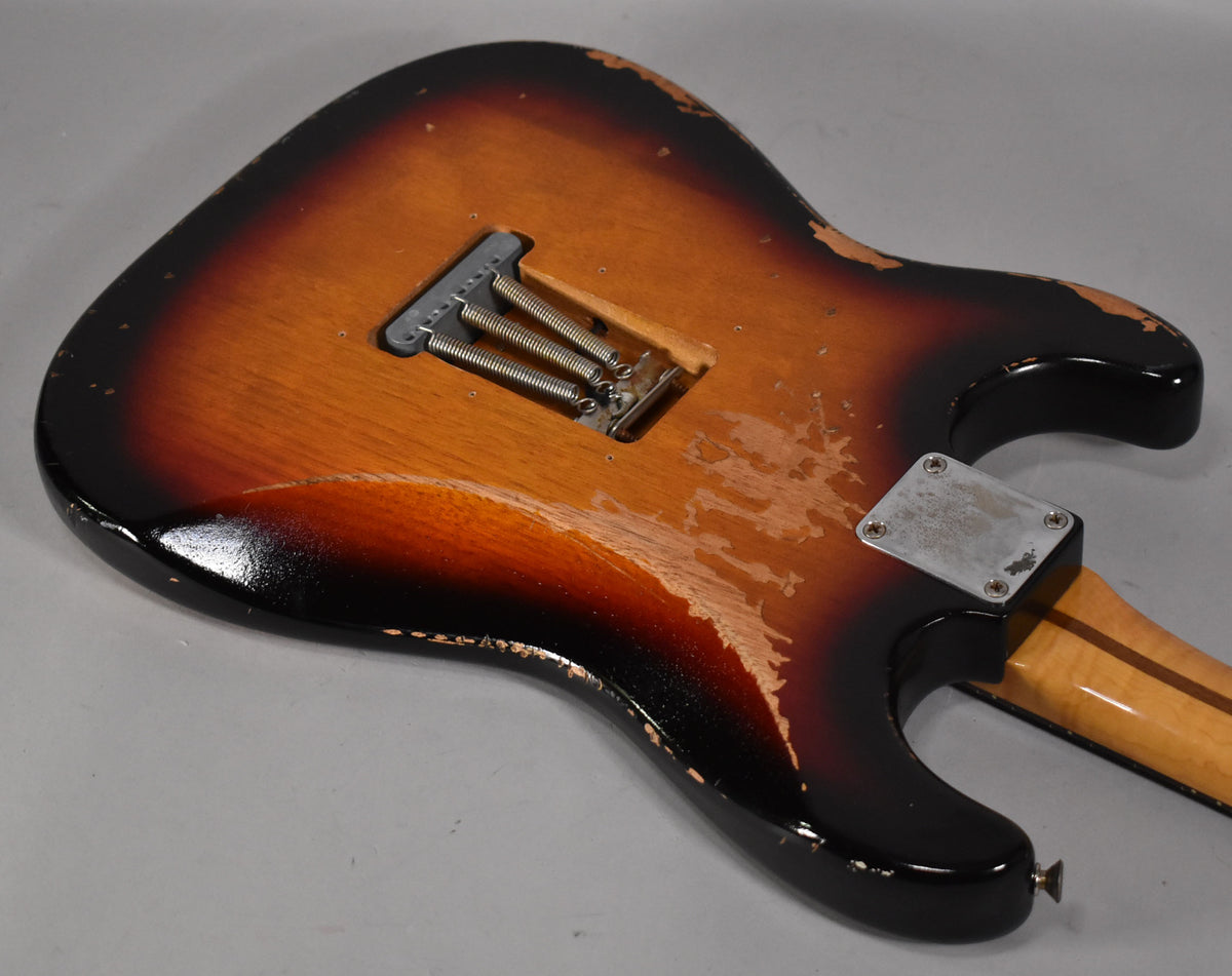 The back of a sunburst S-style guitar body, showing heavy finish wear, a tremolo spring cavity, and a four-bolt neck plate.