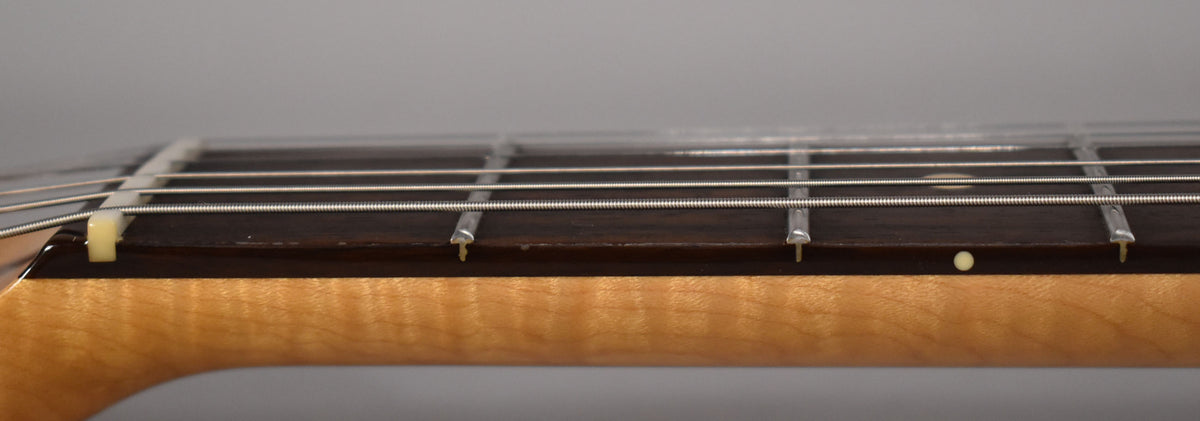 Close-up of the dark rosewood fretboard and maple neck, showing the nut, frets, strings, and a single cream dot inlay.