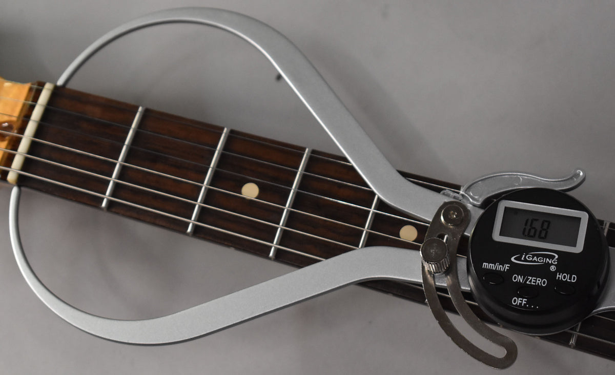Close-up of the dark rosewood fretboard with light fret markers, showing a digital caliper measuring fret height at 1.68.