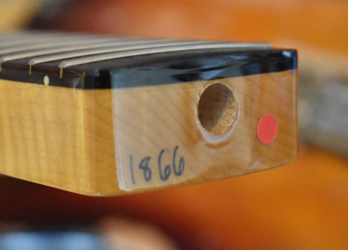 Close-up of the guitar neck heel, showing a circular hole, a red dot, and "1866" written on the light wood.