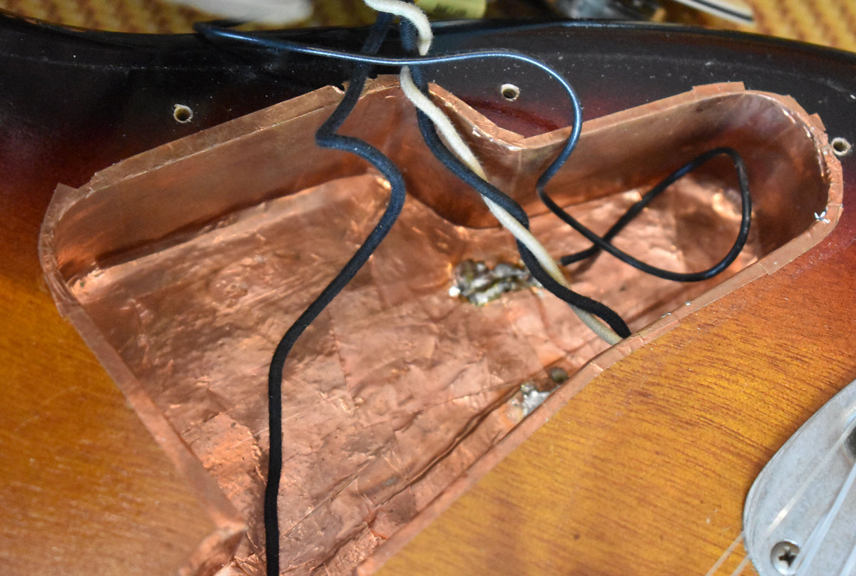 Close-up of the sunburst guitar body, showing the copper-shielded control cavity with black and white wires, and solder points.