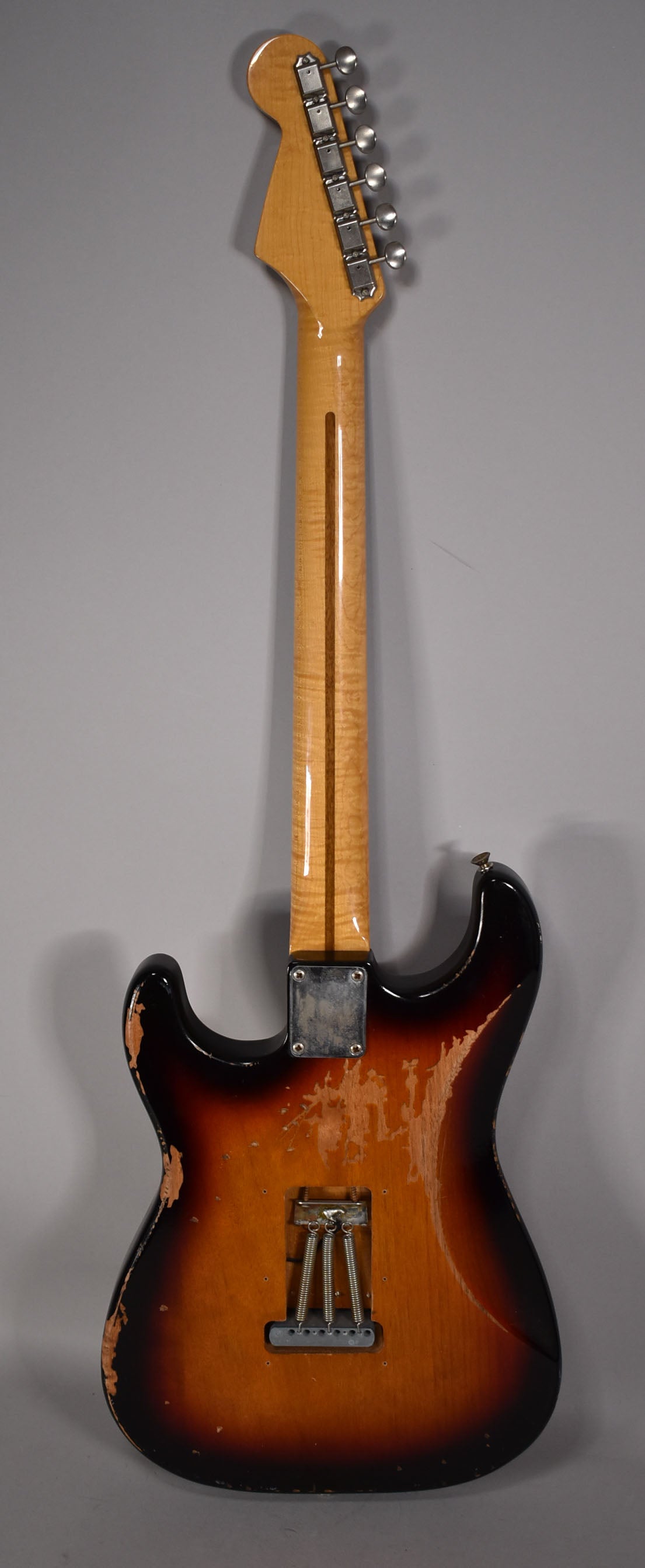 Rear view of a sunburst S-style guitar with heavy relic wear, showing the maple neck, headstock with tuners, and tremolo spring cavity.