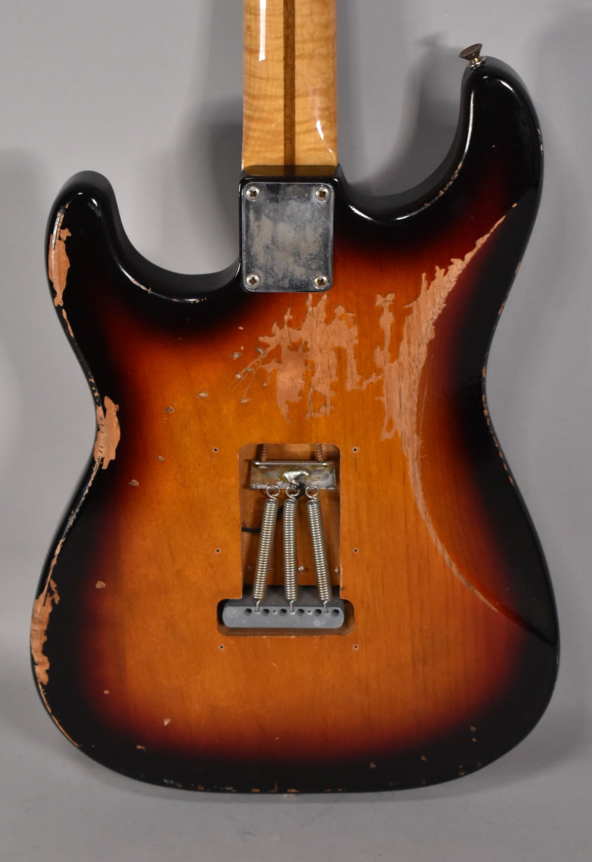 Rear view of a sunburst S-style guitar, showing heavy finish wear, a maple neck, and a tremolo spring cavity with three springs.
