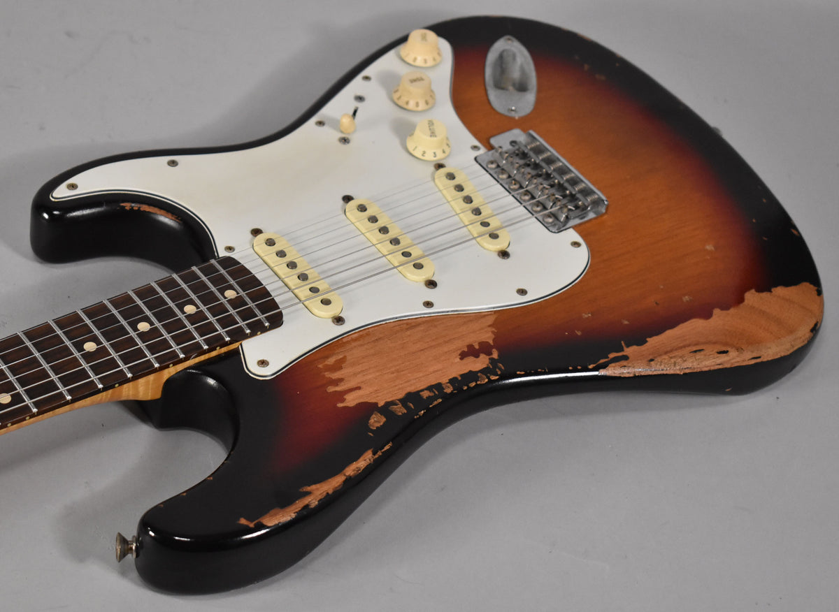 The sunburst S-style guitar body is angled right, showing heavy relic wear on the lower bout, bridge, and pickups.