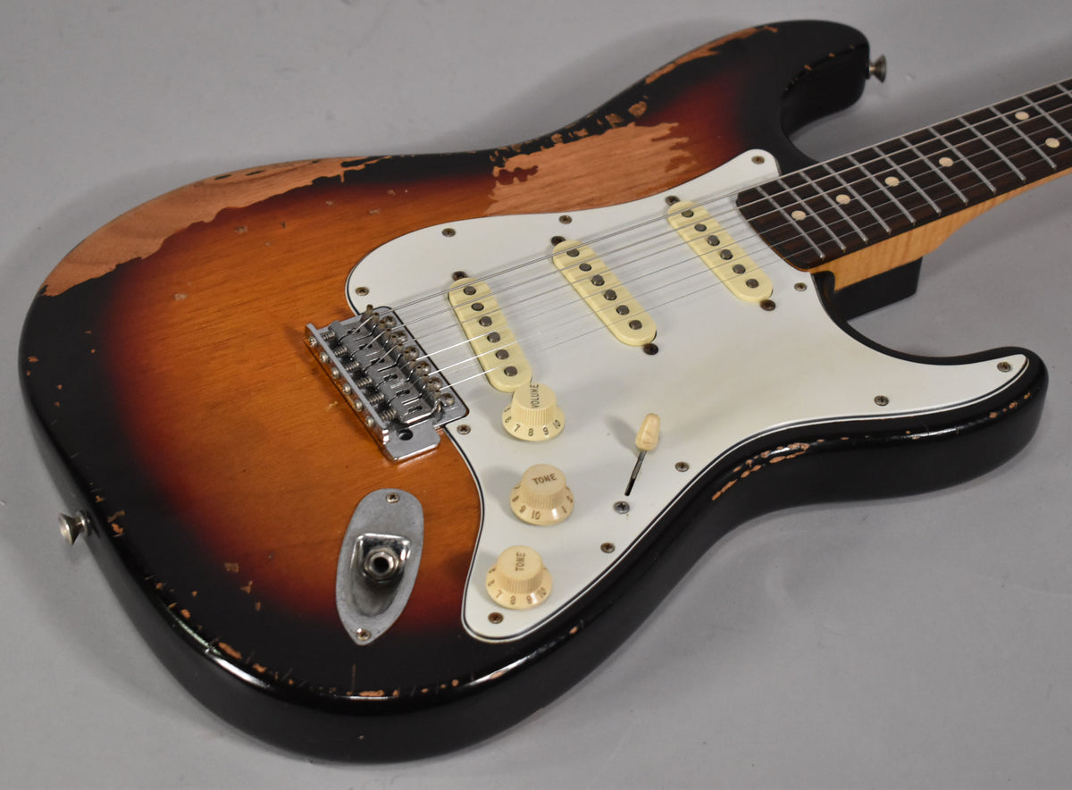 The sunburst S-style guitar body is heavily relic'd, showing exposed wood and wear on the black edges, with cream pickups and controls.
