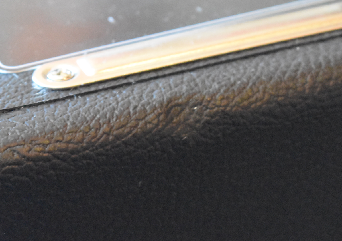 Close-up of the amp's black textured tolex covering, showing a silver metal strip and screw at the top left, with minor scuffs.