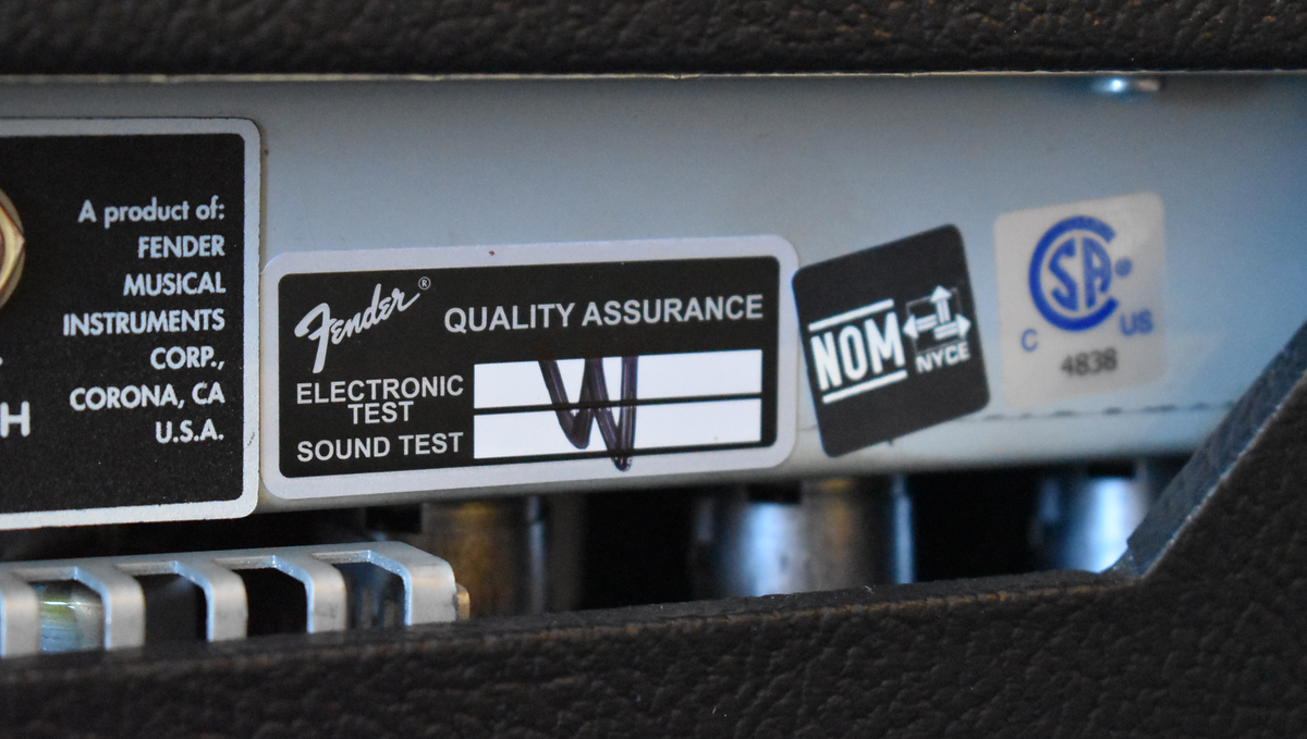 Close-up of the amp's rear panel, showing several black and white compliance stickers, one with a handwritten "W" mark.